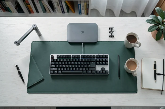 Vue aérienne d'un bureau home office soigneusement organisé avec clavier mécanique, tapis de bureau en cuir vert, chargeur sans fil et accessoires minimalistes