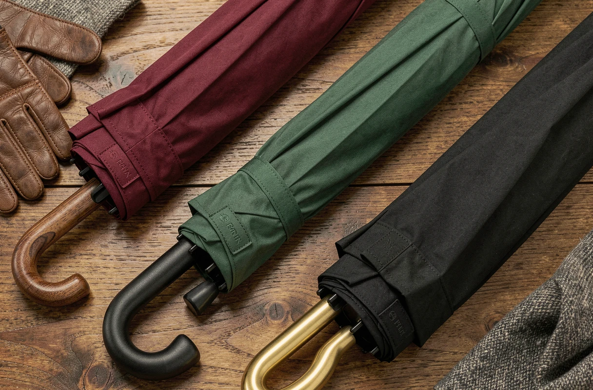 Trois parapluies de marque haut de gamme disposés en flat lay sur une surface en chêne, mettant en valeur différents styles de manches